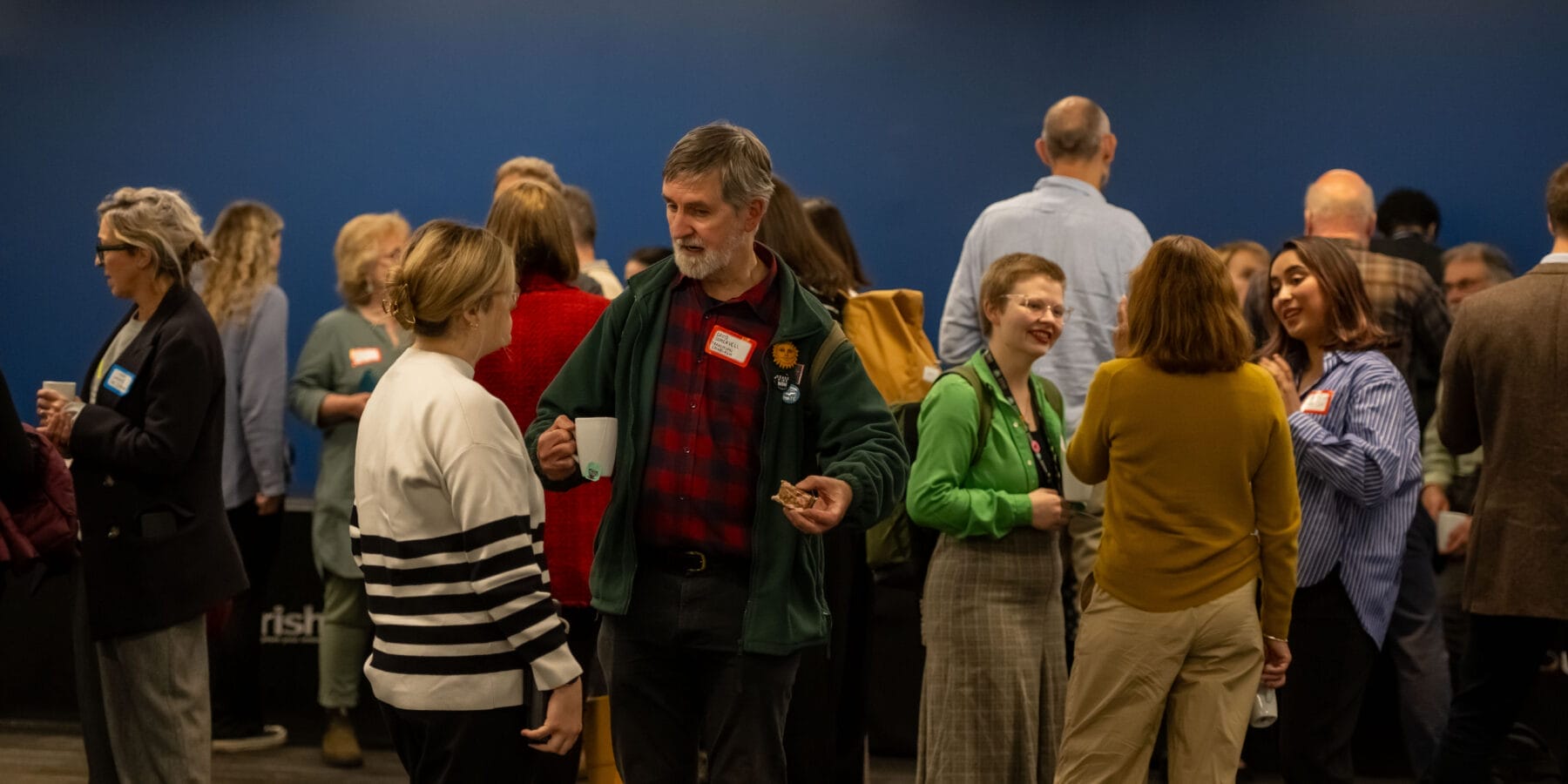 A room of people standing speaking to each other in small groups.
