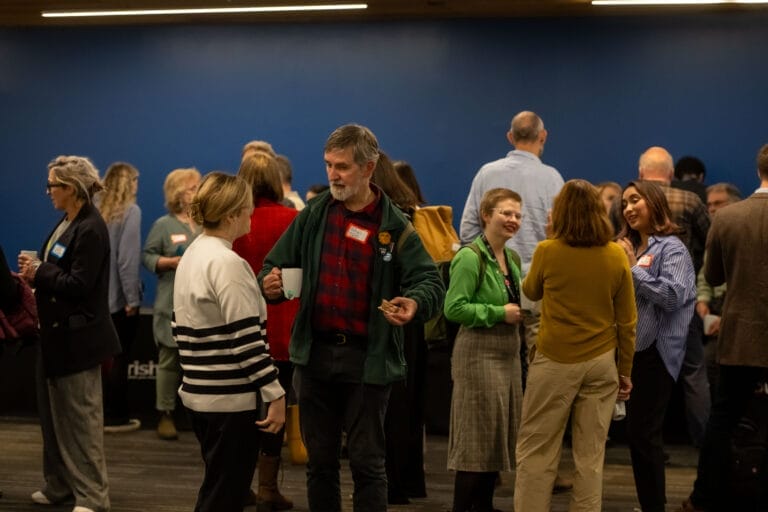 A room of people standing speaking to each other in small groups.